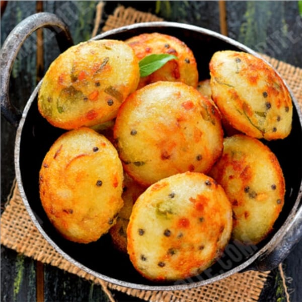 A black bowl filled with golden-brown South Indian paniyaram, garnished with a green leaf.