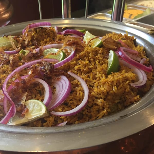 Close-up of Kaveri South Indian Restaurant's biryani, garnished with red onions, fried onions, and lime wedges.