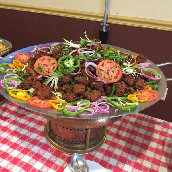 A large platter of Kaveri South Indian chicken 65, garnished with onions, tomatoes, and peppers.