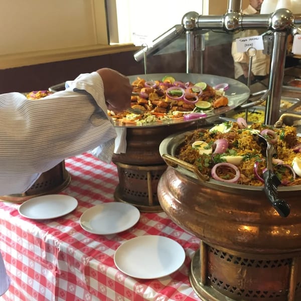 A person serving themselves Indian food from a buffet with biryani and fish dishes.