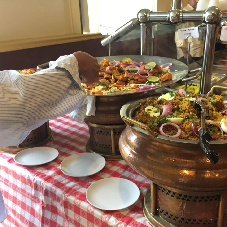 A person serving themselves Indian food from a buffet with biryani and fish dishes.