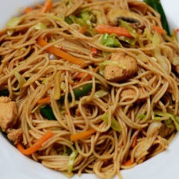 Close-up of Indian noodles with chicken, carrots, and cabbage in a white bowl.