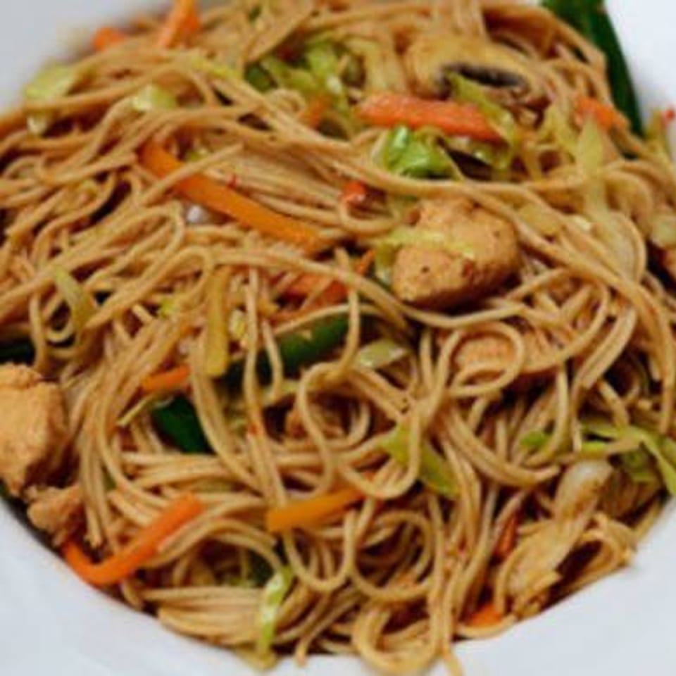 Close-up of Indian noodles with chicken, carrots, and cabbage in a white bowl.