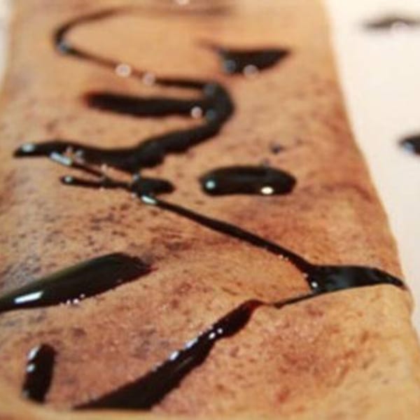 A close-up of a golden-brown dosa drizzled with dark chocolate sauce, a sweet Indian dessert.